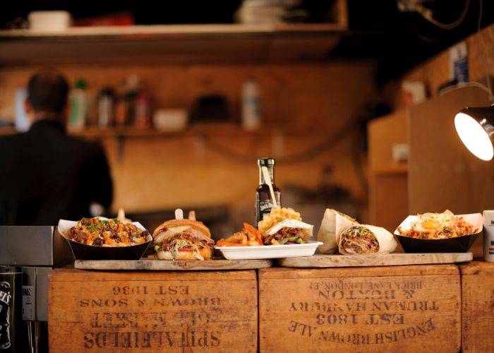 Dishes lined up on the counter of a food truck. In the background, a man works in the kitchen.